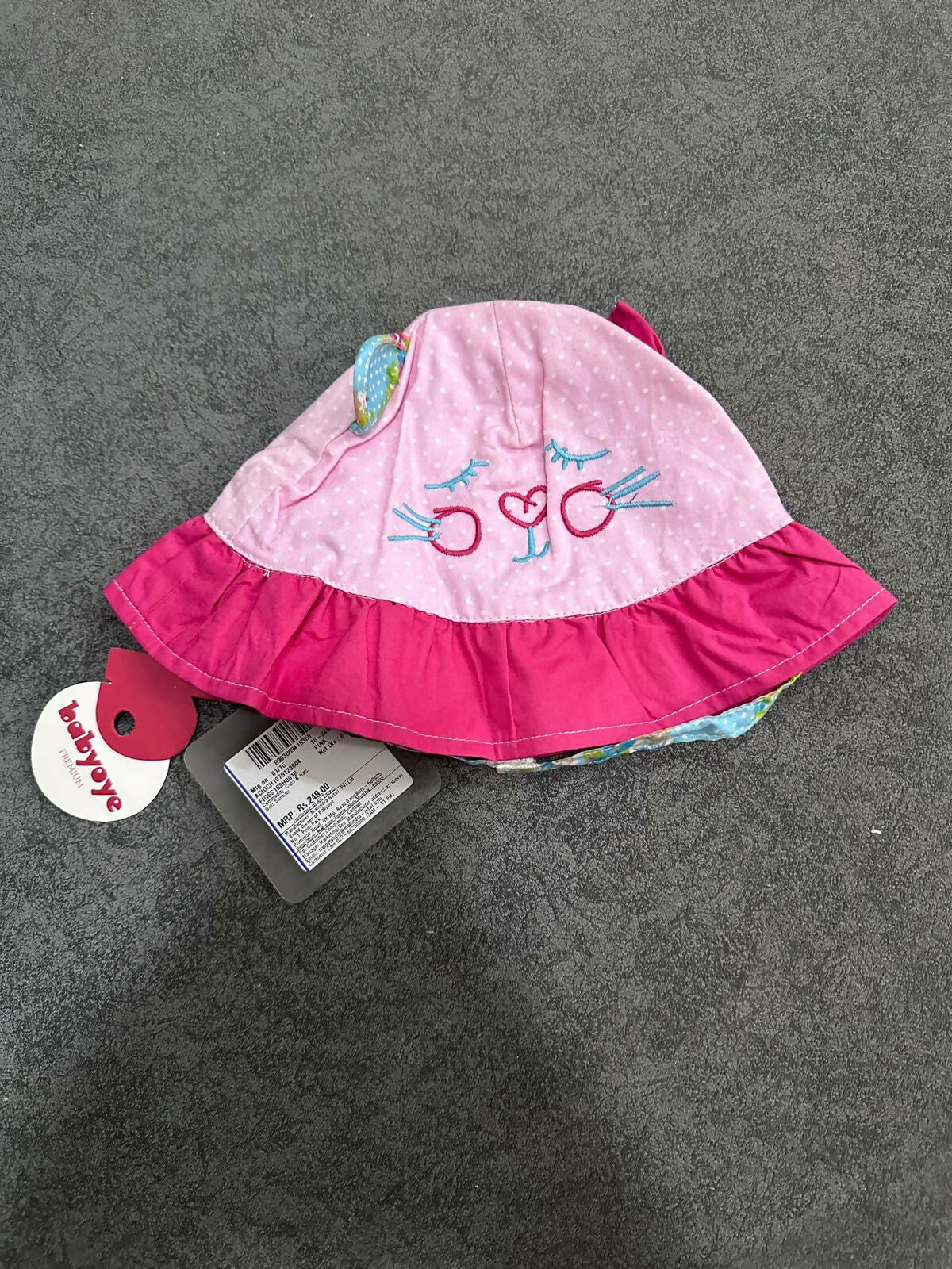 Pink baby hat with ruffled edge on a gray surface