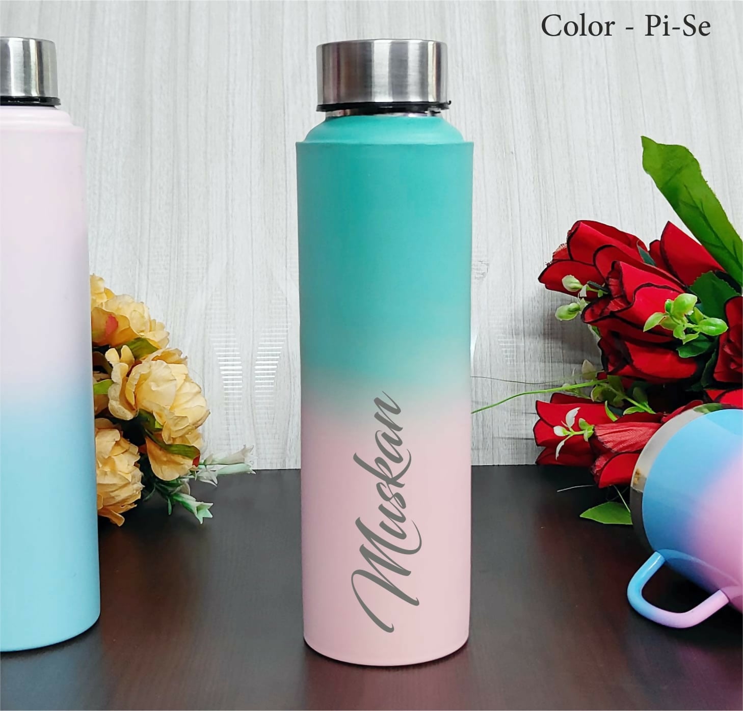 Gradient water bottle transitioning from blue to pink with 'Muskkan' branding, surrounded by flowers.