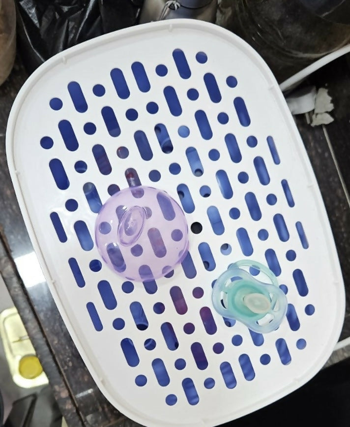 White and blue grid container with two baby pacifiers inside on a dark surface.