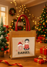 Gift bag with 'DANIEL' printed on it, featuring a cartoon design of a person in a Santa hat and a child, set against a festive background with Christmas trees and lights.