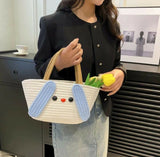 Person holding a white bag with blue bunny ears and a yellow tulip, standing in an indoor setting.