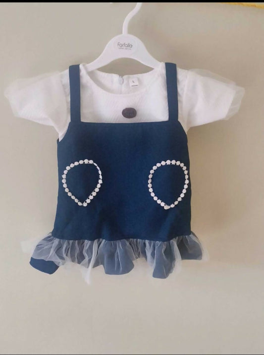 Children's outfit with navy blue dress over white shirt on a hanger against a beige background