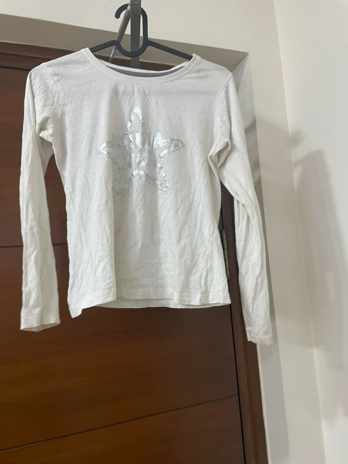 White long-sleeve shirt with a logo on a hanger against a wooden door.