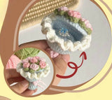 Decorative crochet flower pot with pink flowers held by a hand, on a light background.