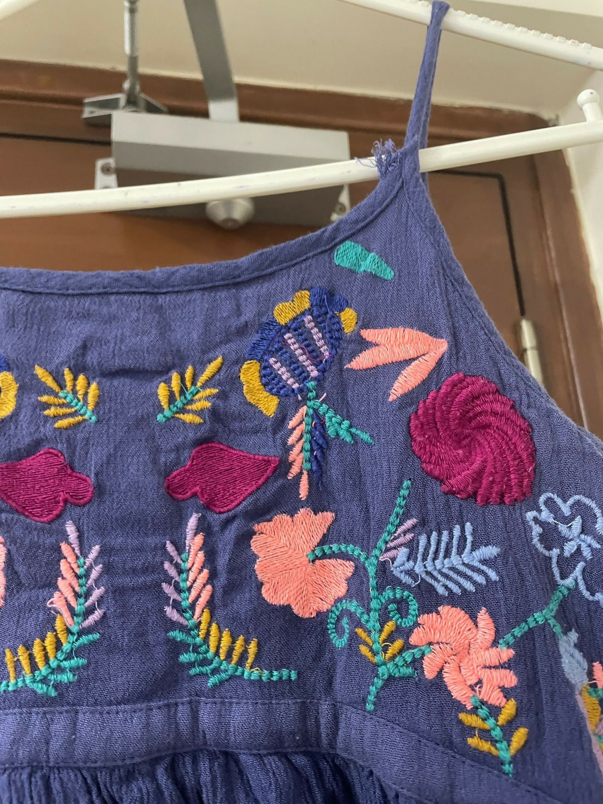 Blue dress with colorful floral embroidery hanging on a rack.