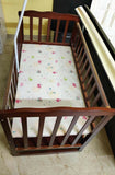 Wooden crib with a colorful mattress cover on a tiled floor.