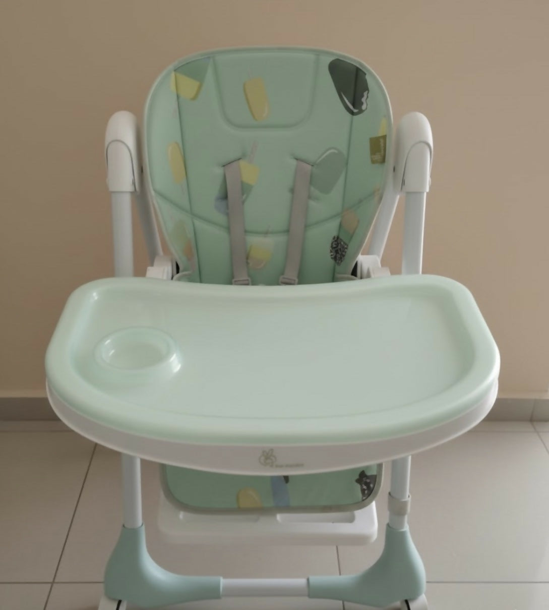 Green and white high chair with butterfly design on a beige background