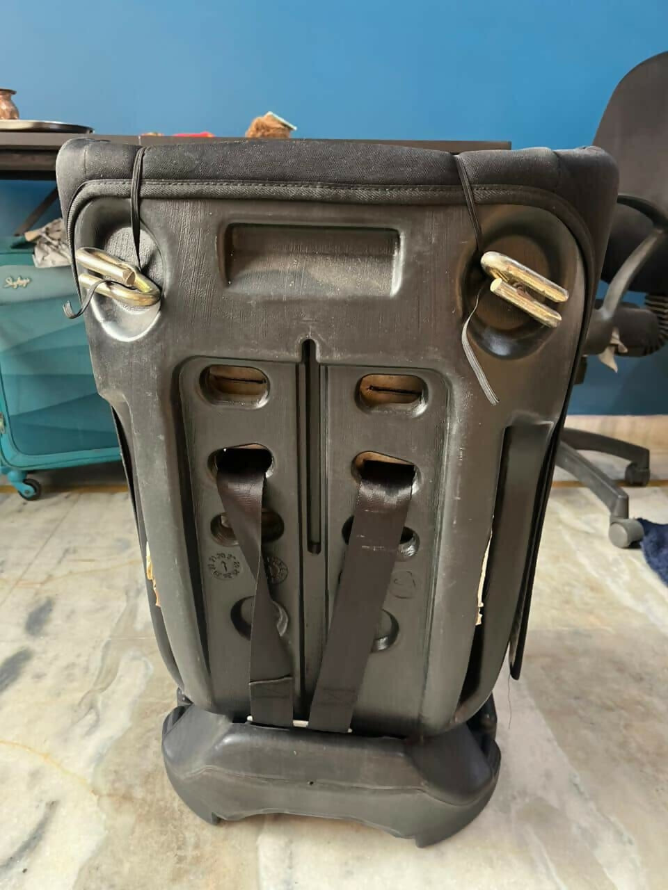 Black metal bracket or support structure on a concrete floor with a blue wall in the background.