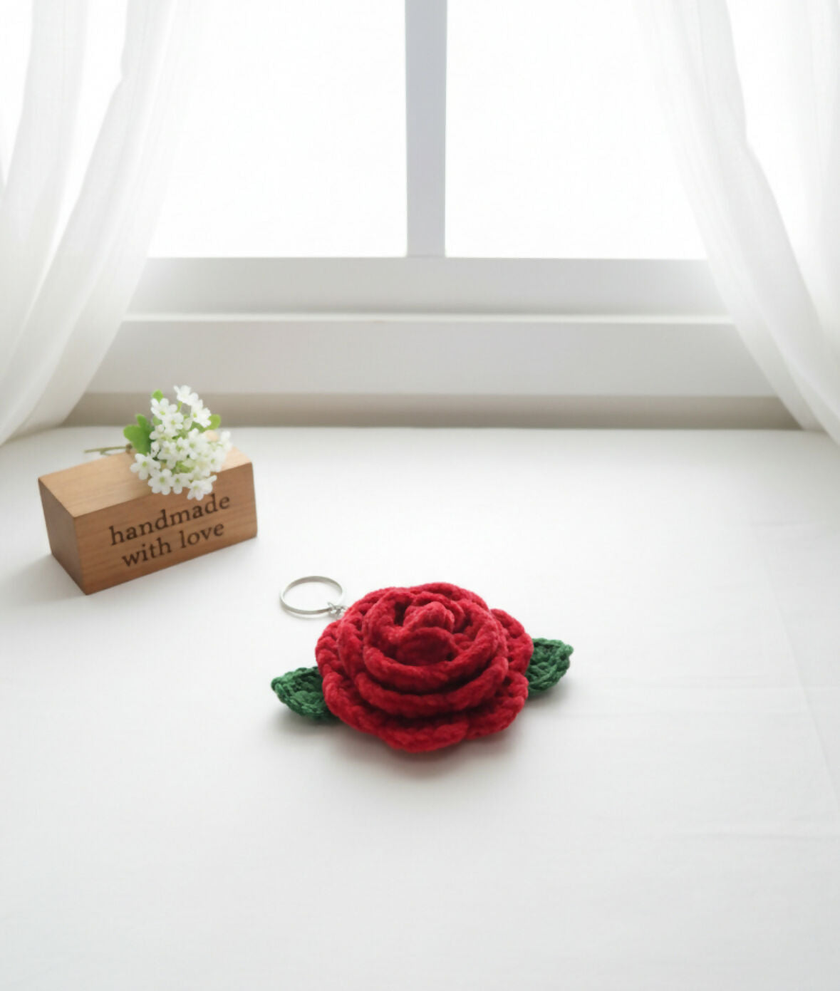 Red rose-shaped keychain on a white surface with a 'handmade with love' sign in the background.