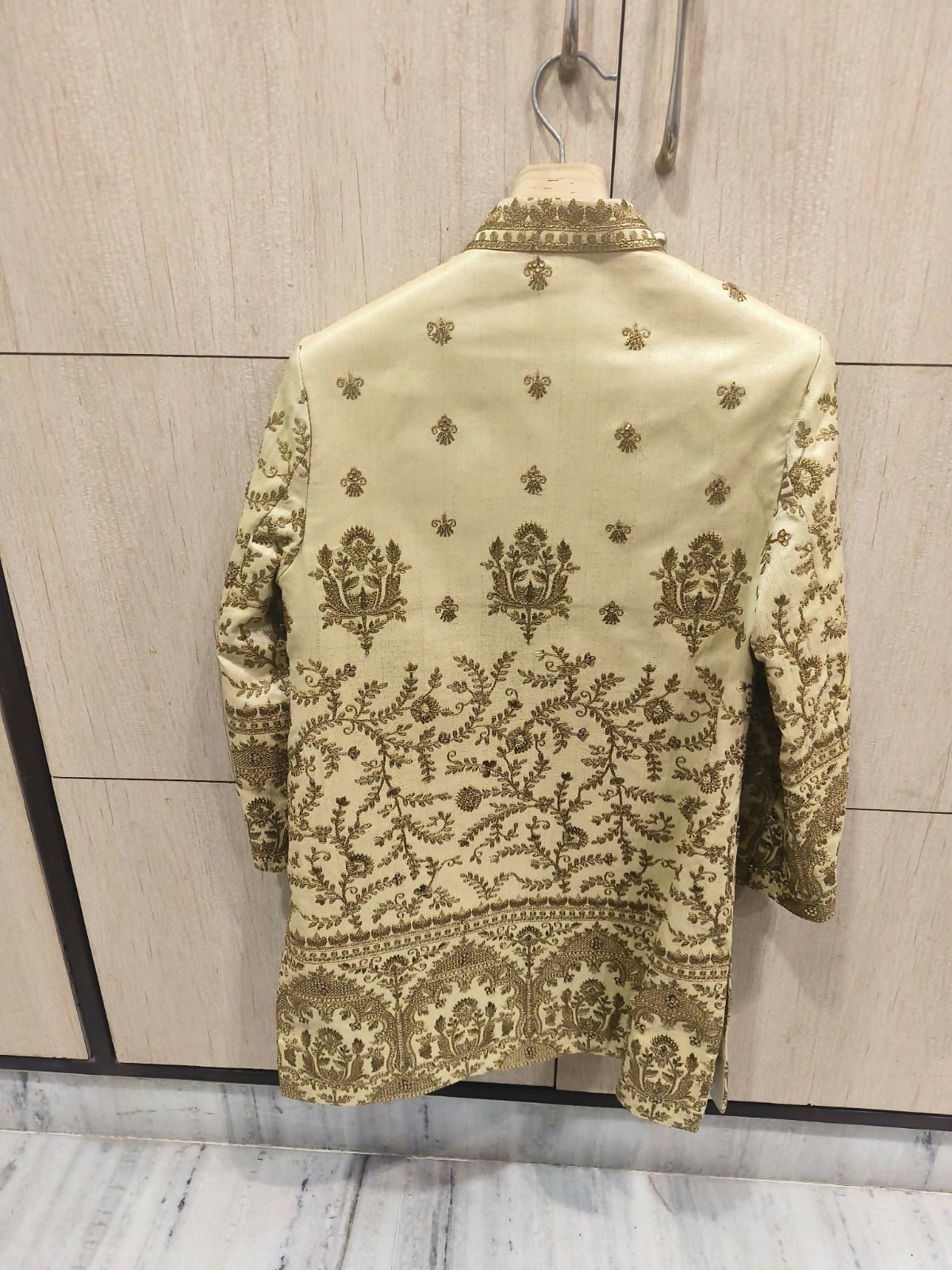 Embroidered traditional outfit on a hanger against a tiled wall.
