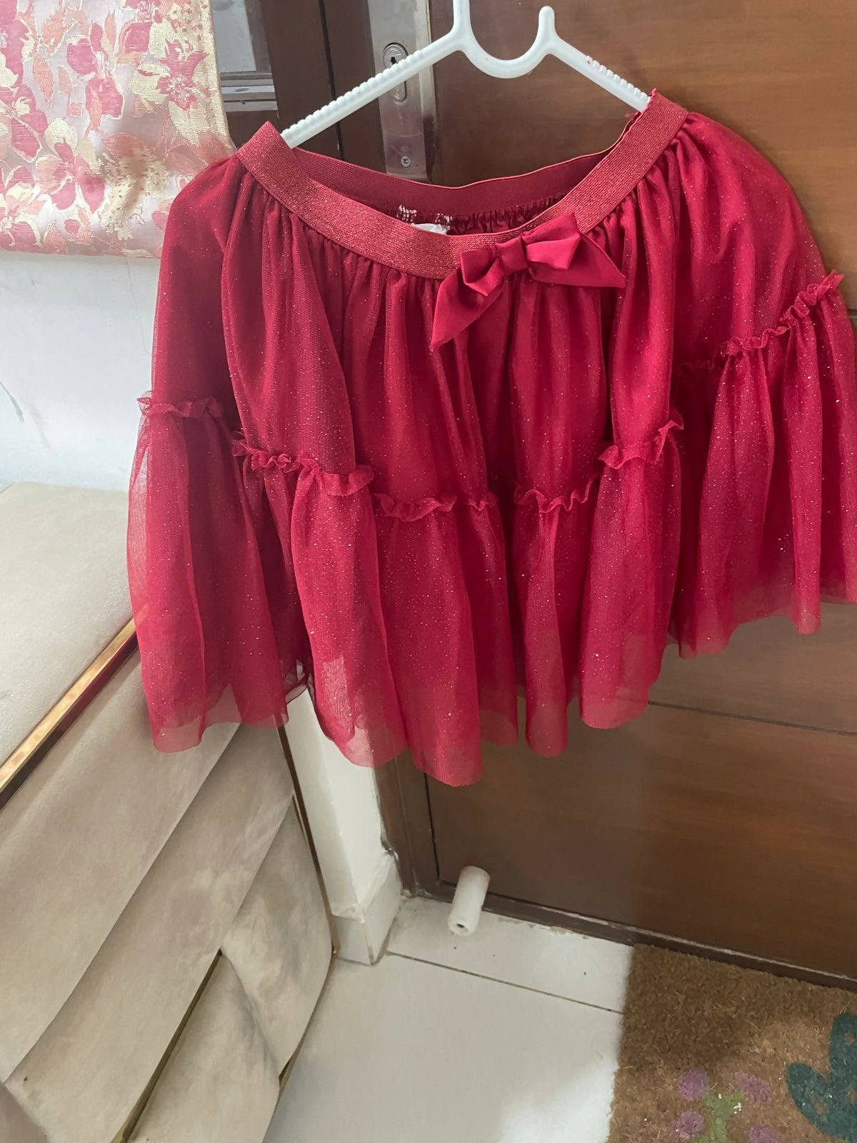 Red blouse with ruffled sleeves and a bow on a hanger against a wooden door.