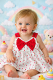 Baby in a polka dot dress with a red bow sitting on a colorful background