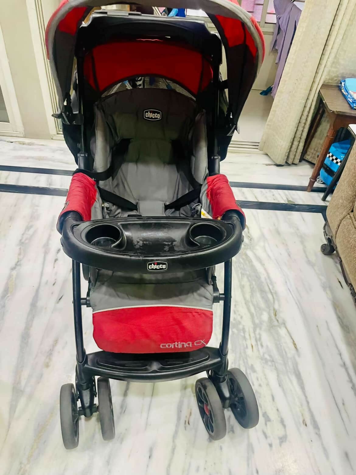 Red and black stroller with 'Cortina' branding on a marble floor.