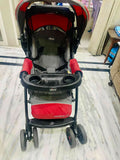 Red and black stroller with 'Cortina' branding on a marble floor.