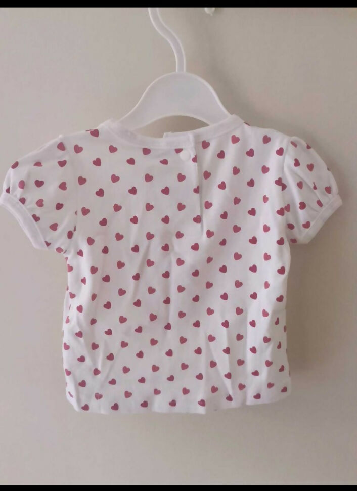 White baby shirt with pink heart pattern on a hanger against a white wall