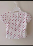 White baby shirt with pink heart pattern on a hanger against a white wall