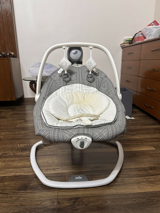 Baby swing with white cushion on a wooden floor in a room setting