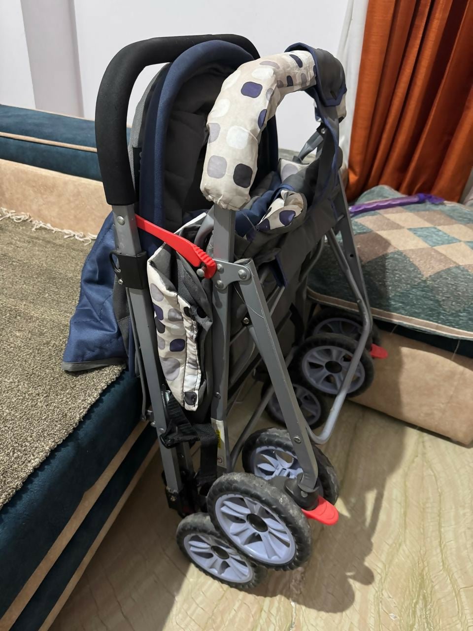 Foldable stroller with patterned seat cover on a wooden floor.
