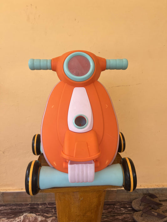 Orange toy scooter with blue handlebars on a wooden surface against a beige wall.