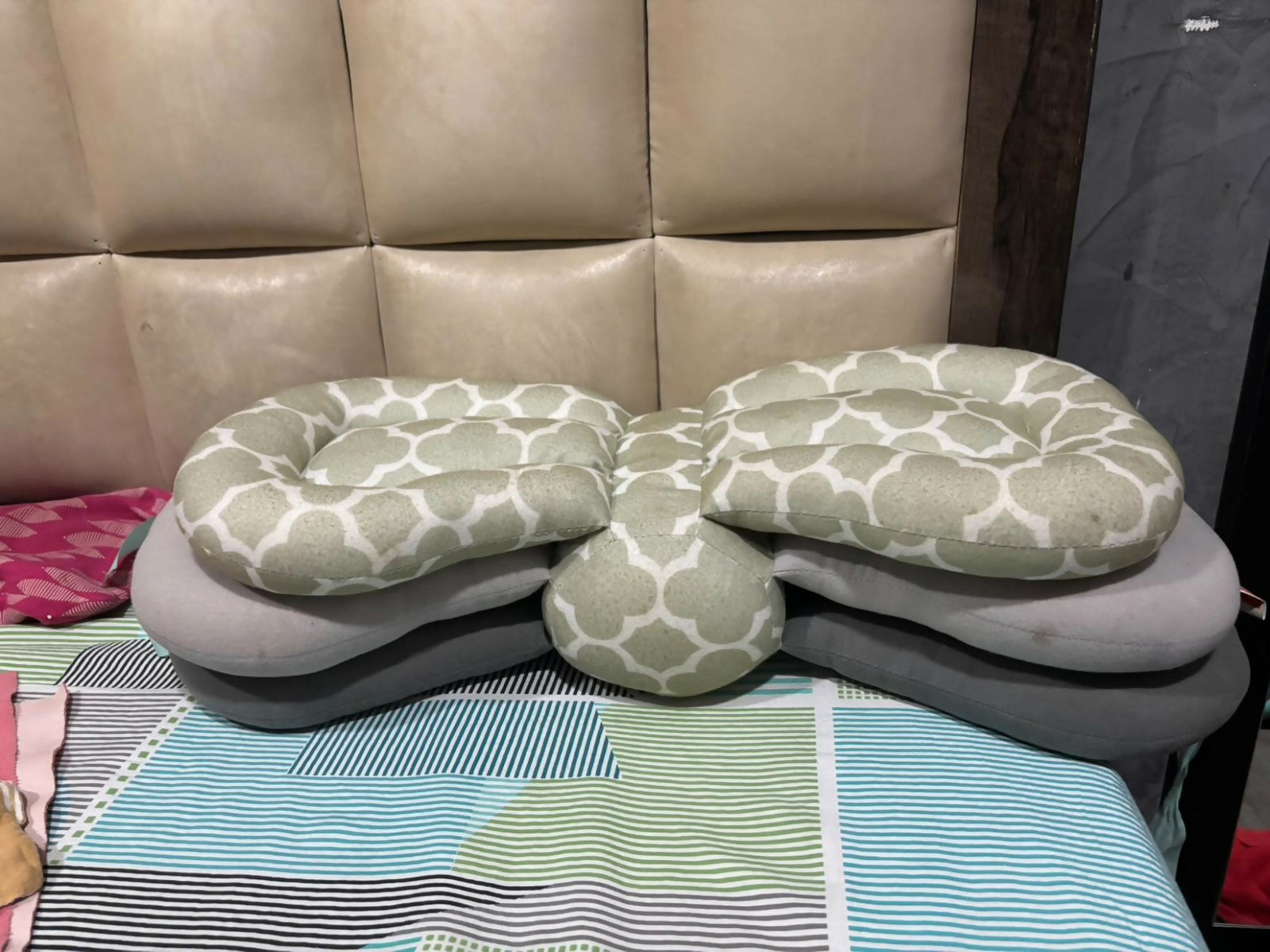 Stack of green and gray patterned pillows on a bed with a beige headboard.