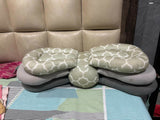 Stack of green and gray patterned pillows on a bed with a beige headboard.