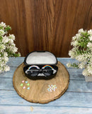 Sunglasses with decorative elements in a case on a wooden coaster with flowers in the background