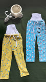 Two pairs of pajama pants, one yellow and one blue with airplane pattern, on a dark surface.