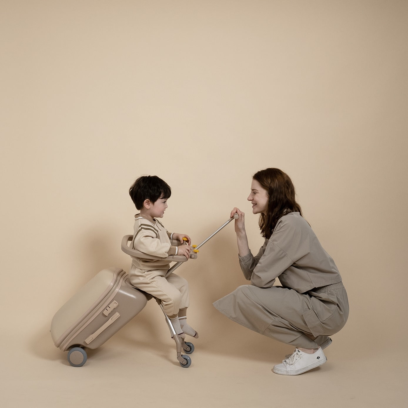 Woman and child playing with a suitcase against a beige background