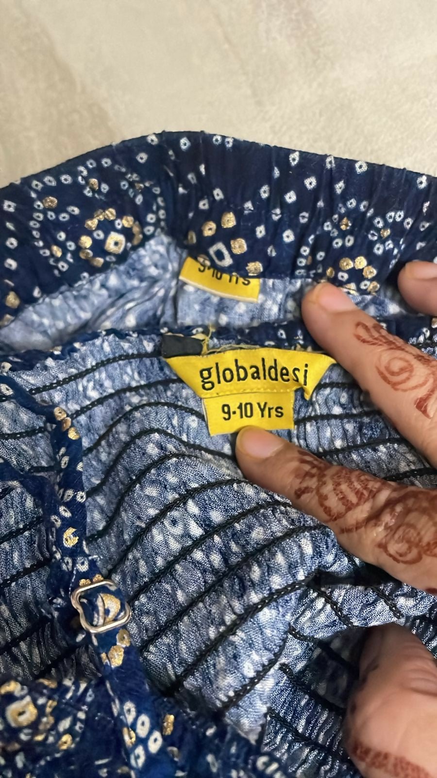 Clothing with a 'globaldes' size label indicating 9-10 years, held by a hand.