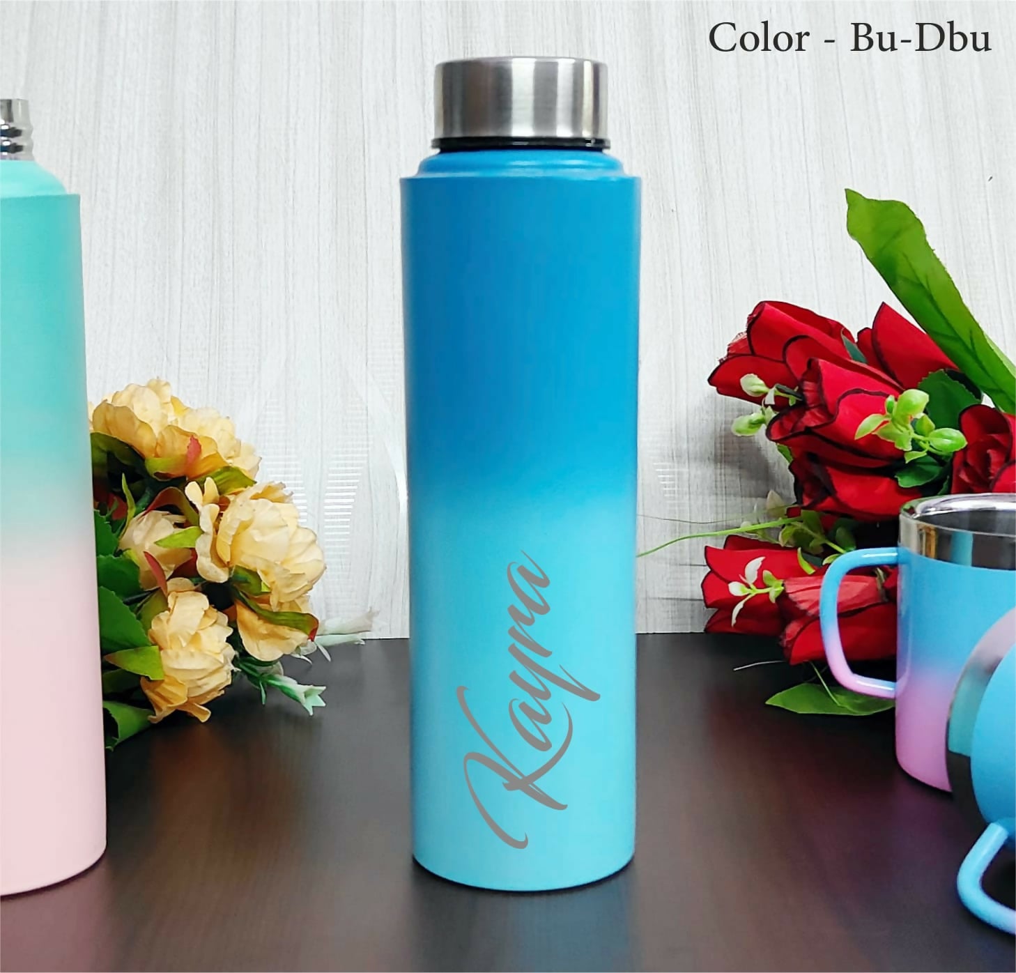 Blue water bottle with 'Kayla' engraving on a wooden surface with flowers in the background