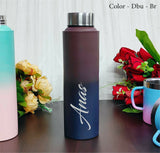 Gradient water bottle with 'Anas' branding on a wooden surface with flowers in the background