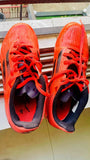 Red athletic shoes with black soles on a wooden surface