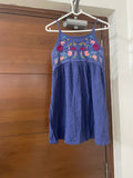 Blue dress with floral embroidery on a hanger against a wooden door.