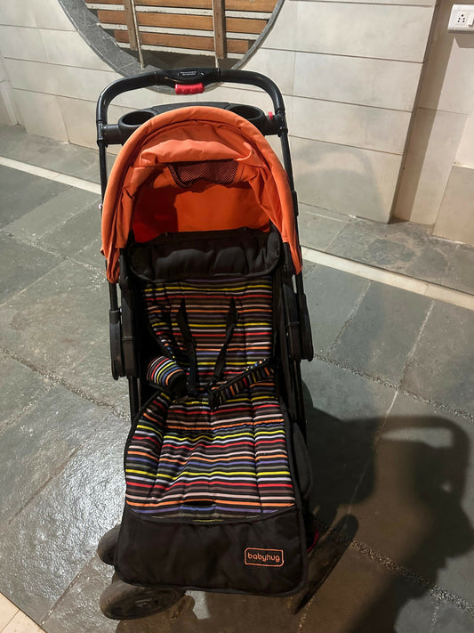 Baby stroller with orange cover and striped seat on a stone floor.