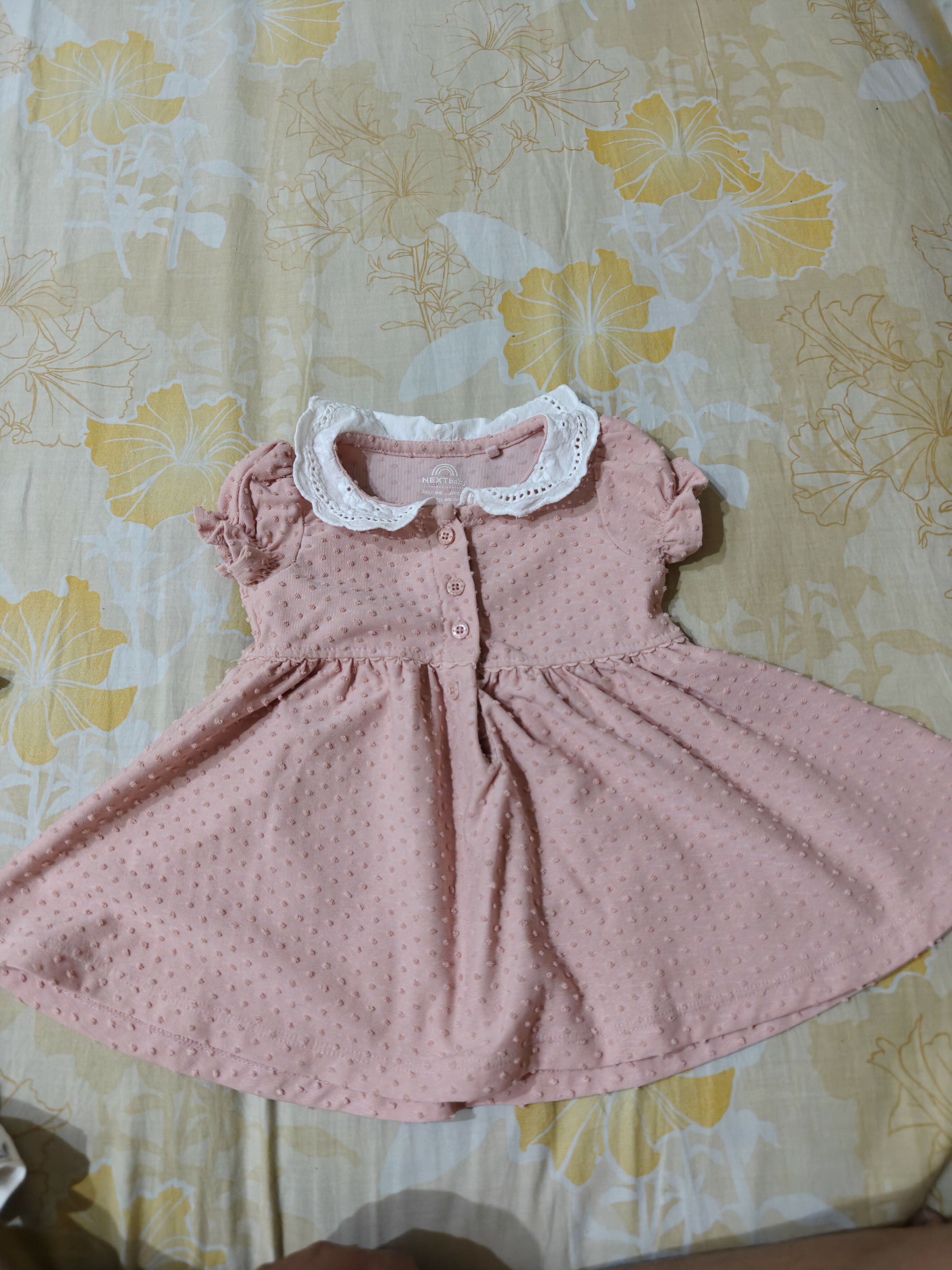 Pink dress with white collar on a floral-patterned surface