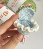 Hand holding a small crocheted ring box with a ring inside, against a blurred background.