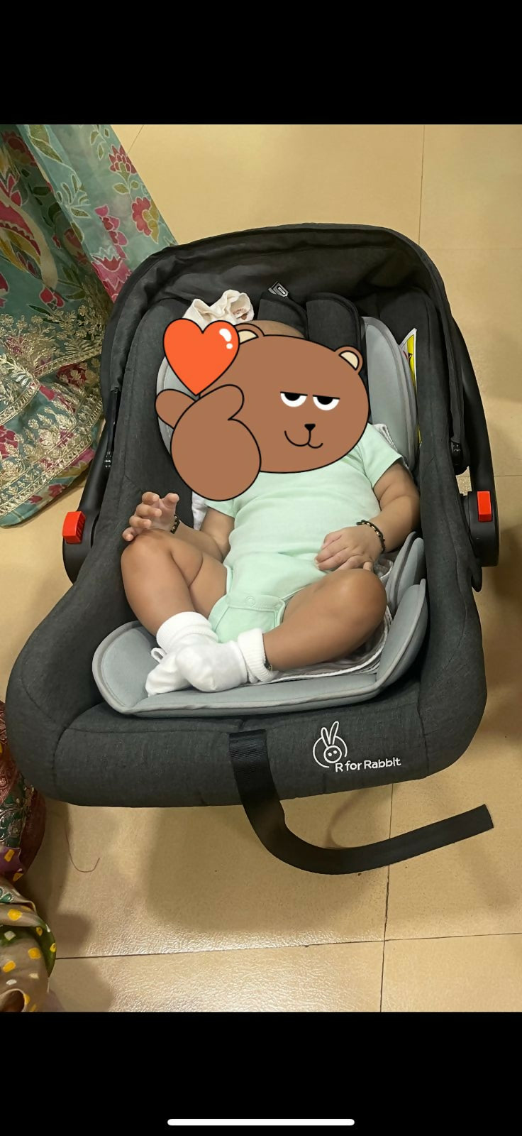 Child in a car seat with a cartoon bear design on a beige floor.
