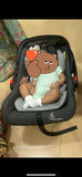 Child in a car seat with a cartoon bear design on a beige floor.