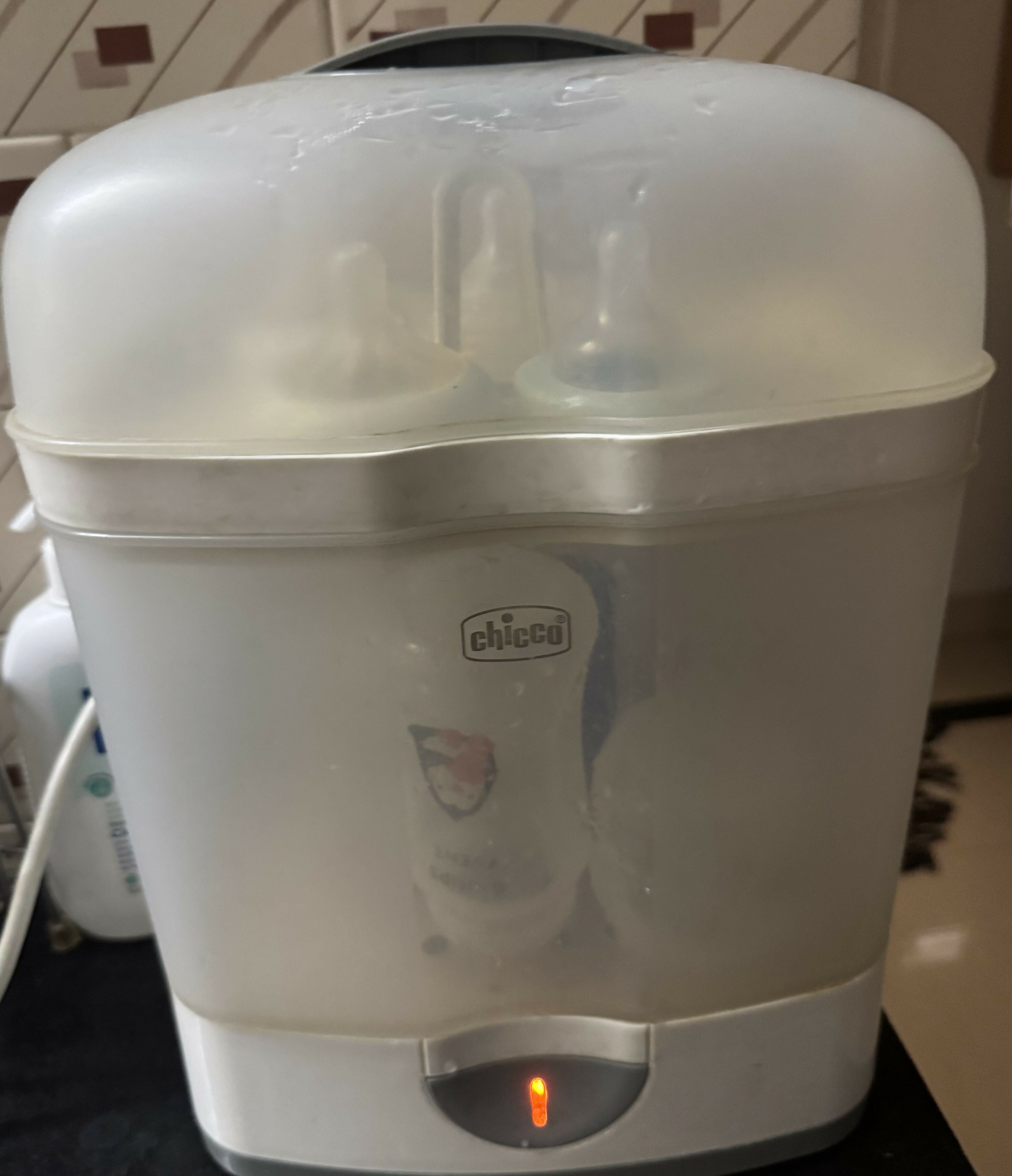 White baby bottle sterilizer with 'Chicco' branding on a dark surface.