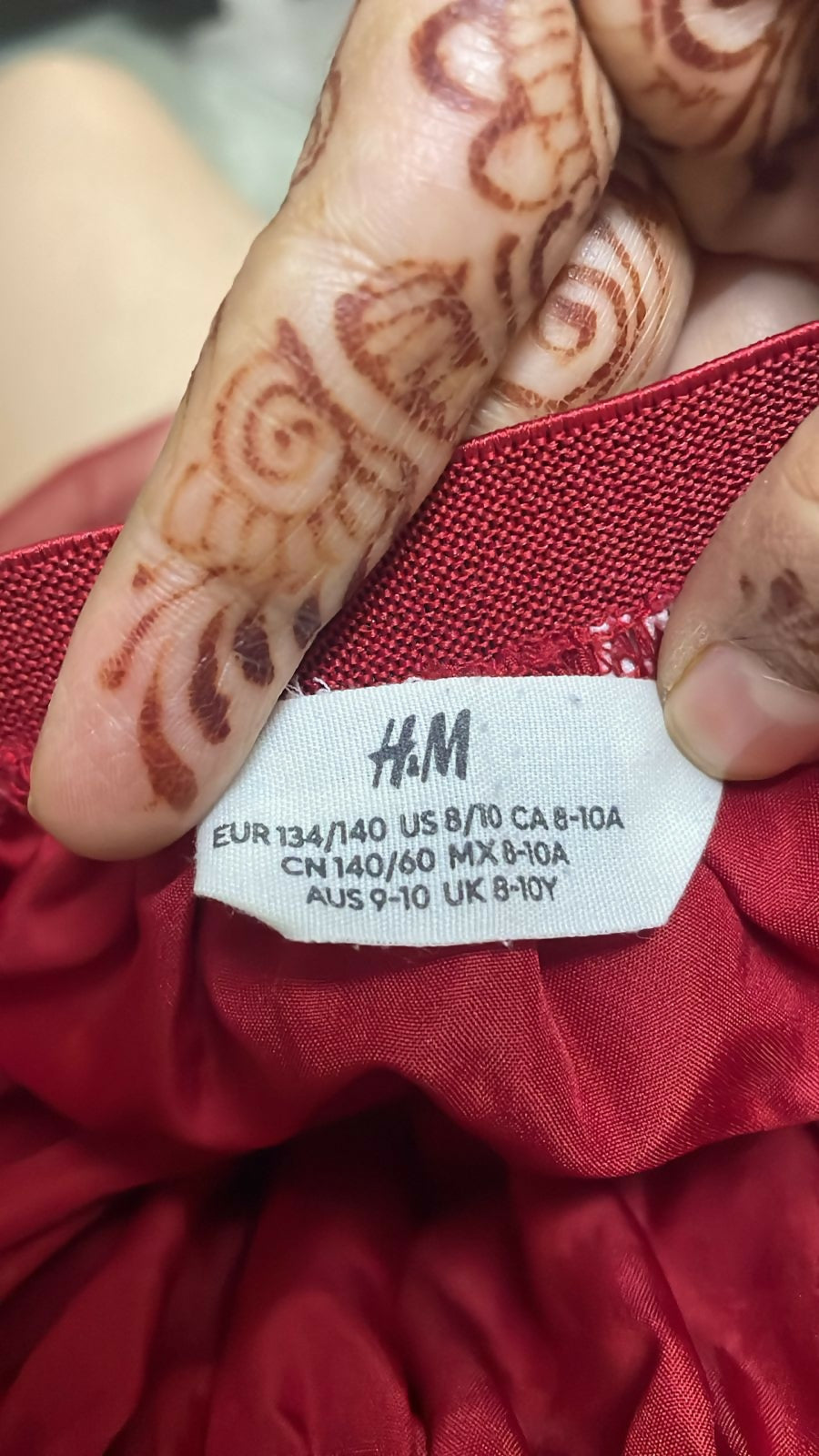 Red garment with an H&M label and hand with henna designs.