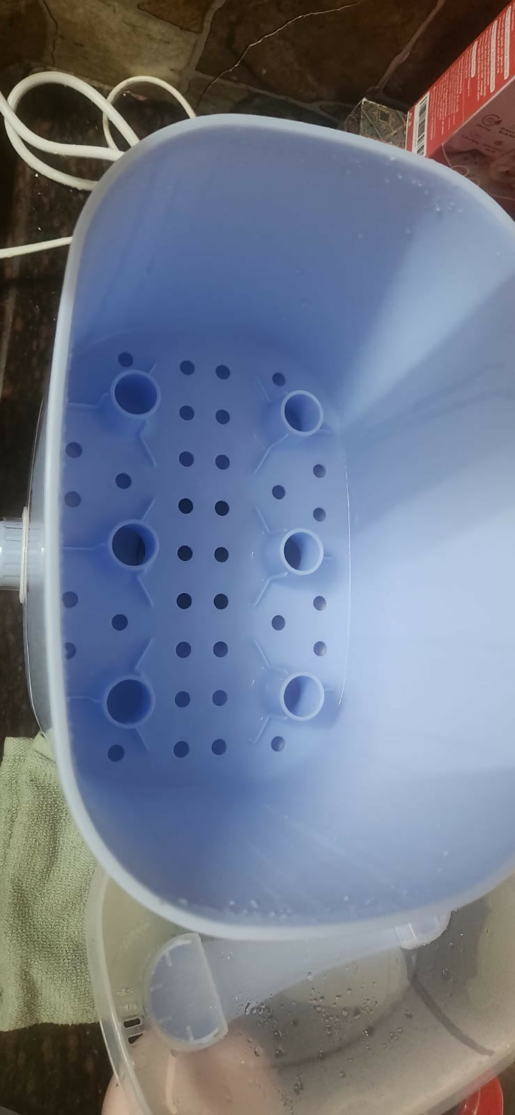 Blue plastic strainer with holes held by a hand on a brown surface