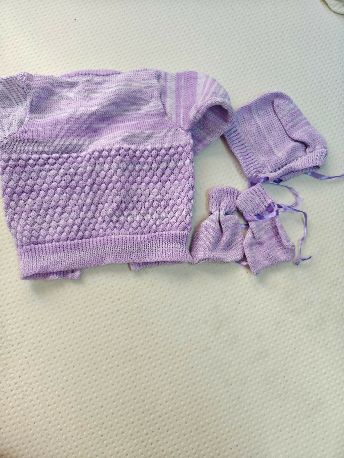 Purple knitted baby outfit with a hat on a light gray background