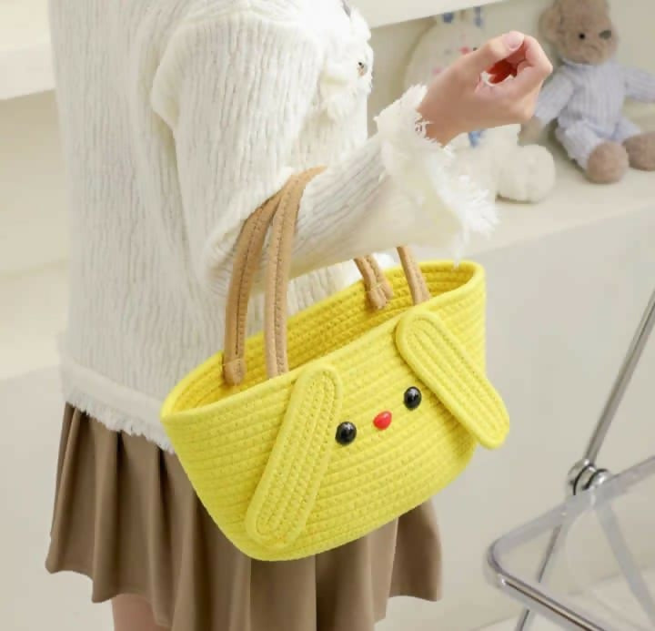 Person holding a yellow knitted bag shaped like a dog with a teddy bear in the background.