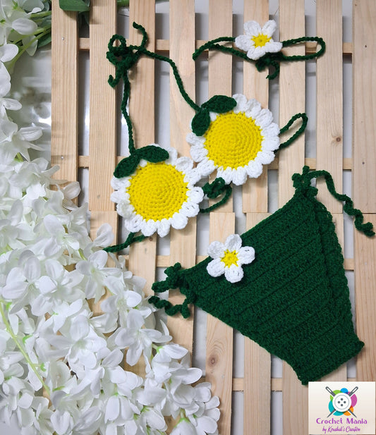 Crocheted daisy flowers and green leaves with white flowers.