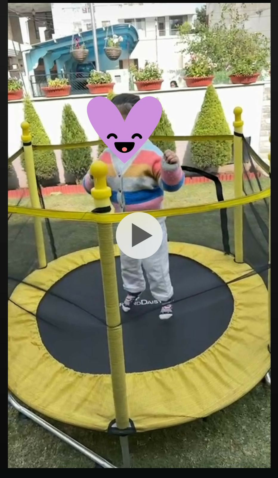 Child on a small trampoline with a colorful heart-shaped cutout in front of a building.