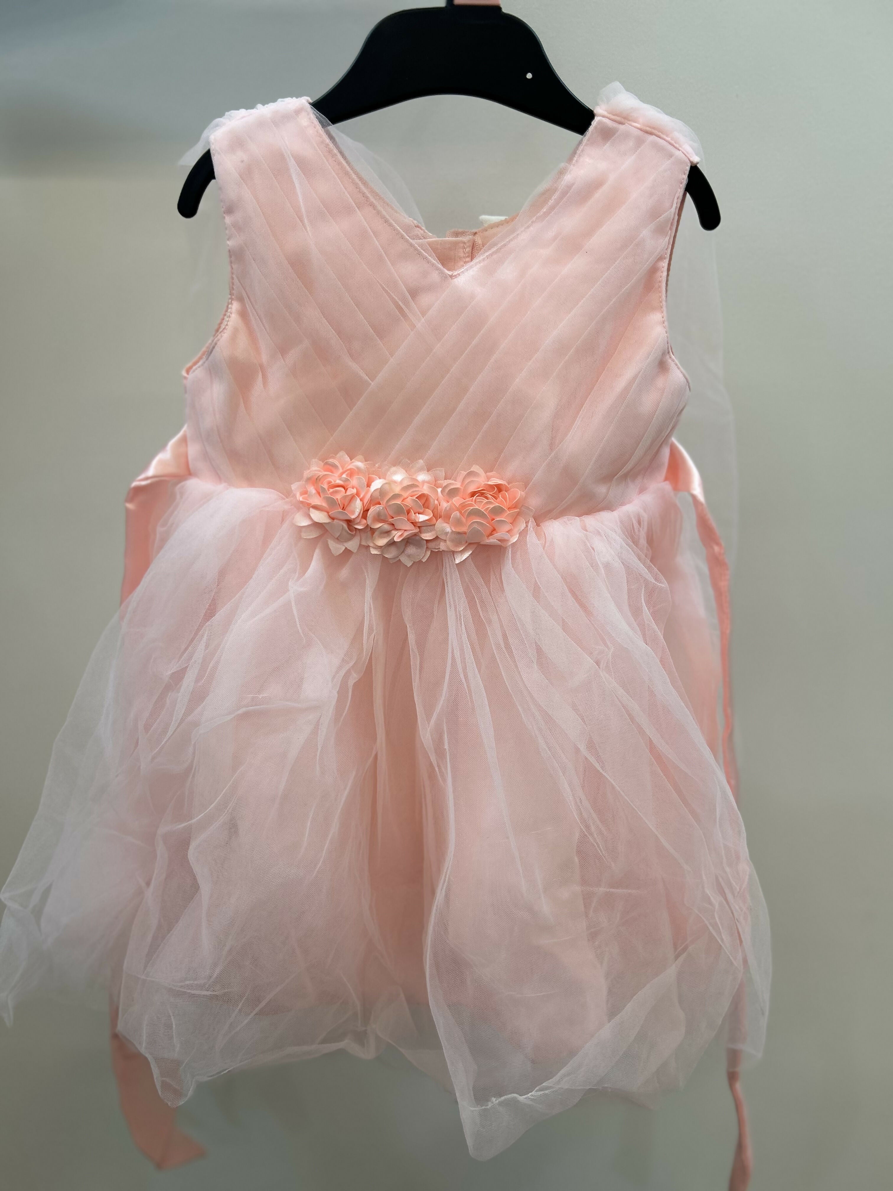 Pink dress with floral embellishment on a hanger against a plain background