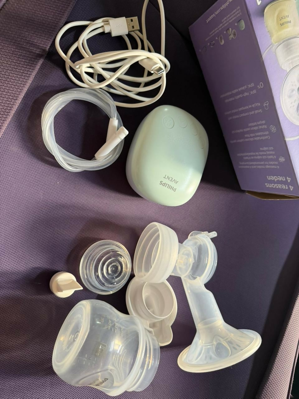 Breast pump parts on a purple surface with packaging in the background