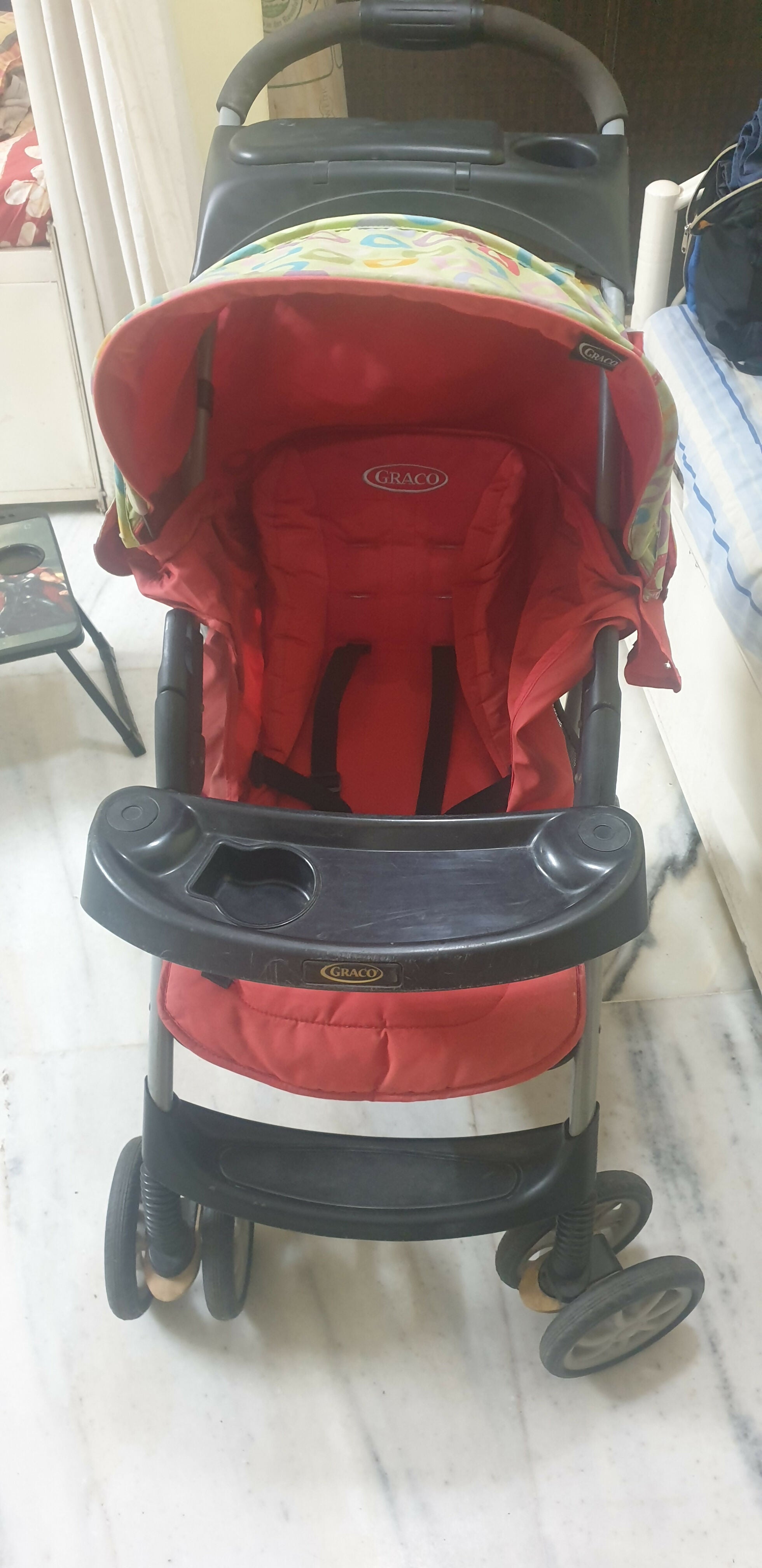 Red and black stroller with floral pattern on a white floor.