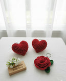 Red heart-shaped and rose-shaped crochet items on a white surface with a 'Handmade with Love' sign.