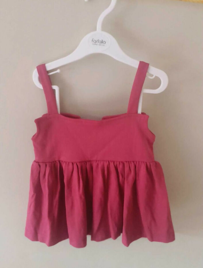 Pink tank top with straps on a white hanger against a beige background